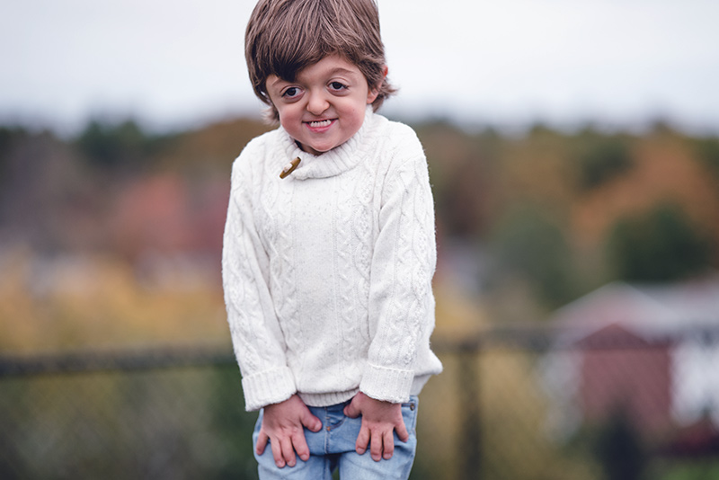 Un jeune garçon souriant avec ses mains sur le sien sur le devant de ses jambes.